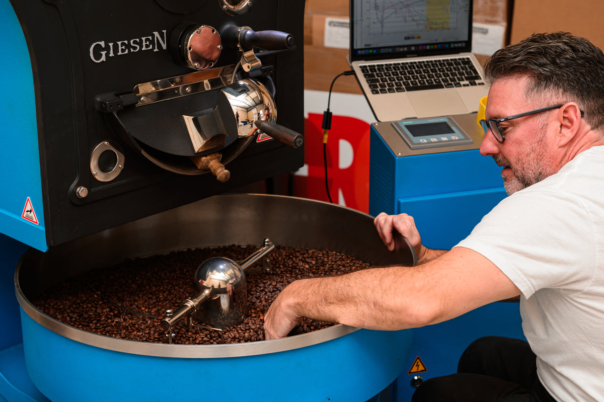 John operating a GIESEN coffee roaster with a laptop nearby